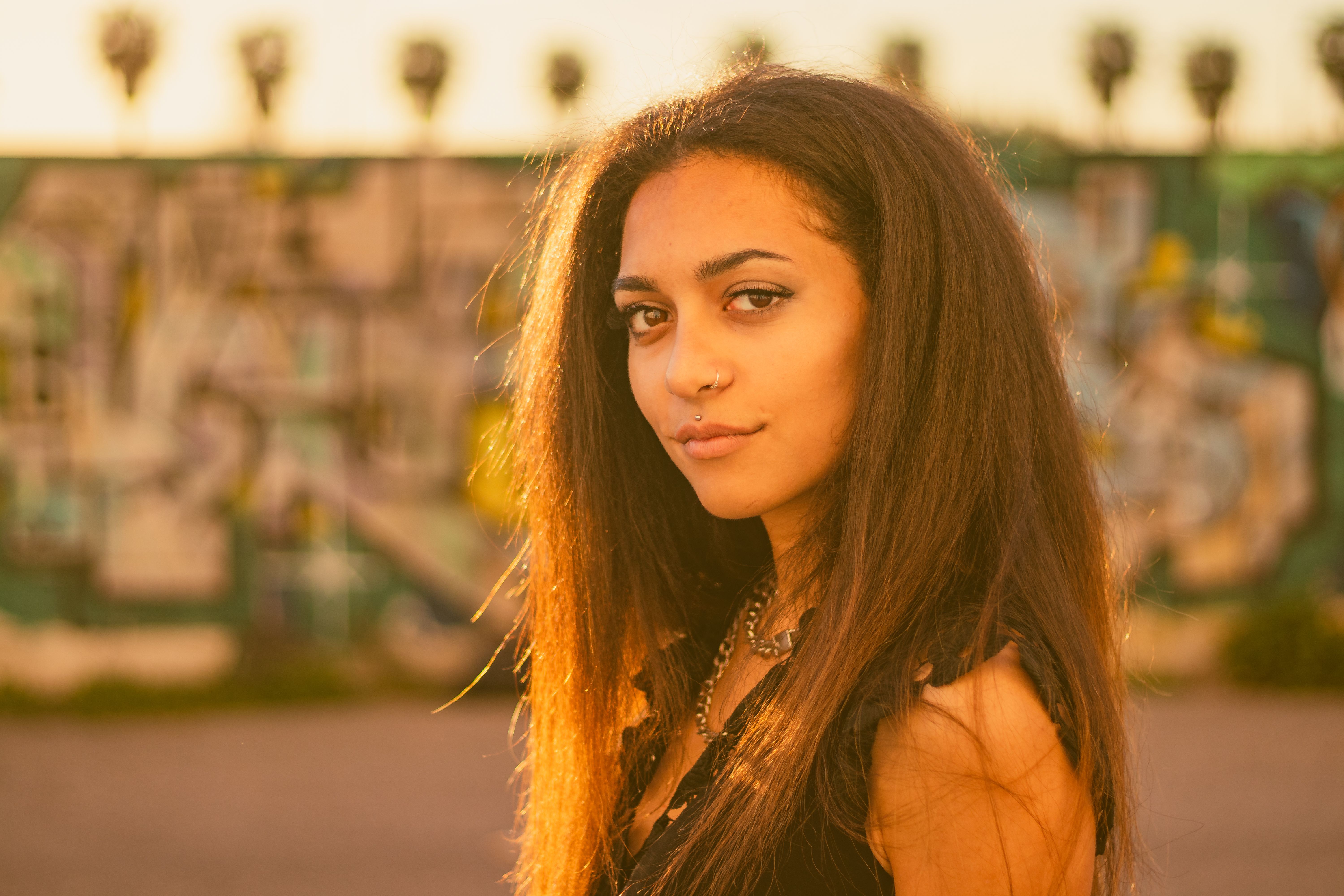 Stylish young woman in Valencia, Spain, poses outdoors against a vibrant graffiti wall.