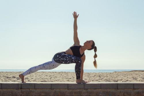 Free Woman performing a yoga pose on a sunny beach, demonstrating flexibility and balance. Stock Photo