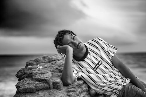 Grayscale Photo of a Man Reclining on the Rock