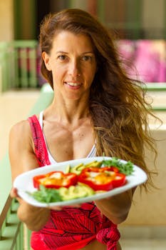 Smiling woman holding a plate with healthy stuffed bell peppers, offering a vibrant and nutritious meal.