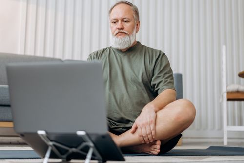 Free Senior man using a laptop for an online meditation session at home. Stock Photo