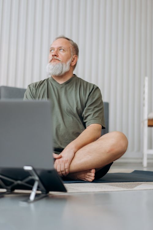 Free Elderly man with beard sitting cross-legged using a laptop, enjoying a moment of relaxation indoors. Stock Photo