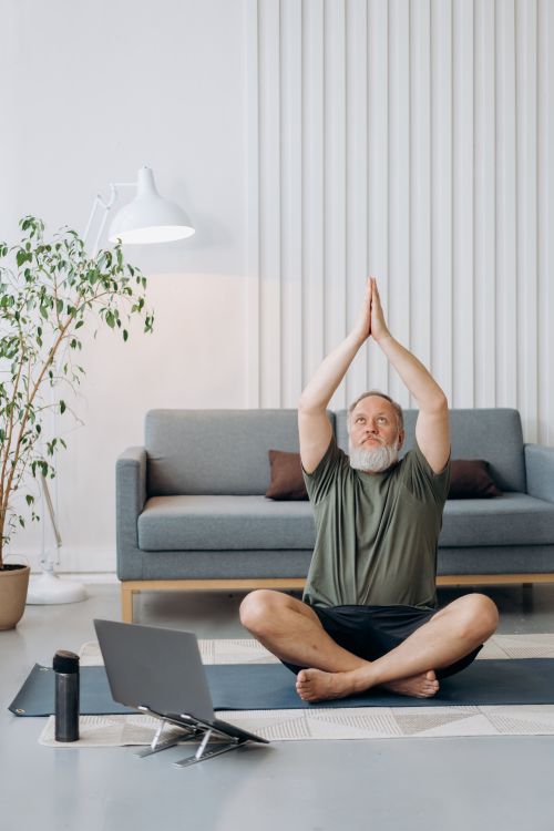 Free Senior man meditating on yoga mat in living room, embracing a healthy lifestyle. Stock Photo