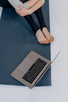 A person sits on a yoga mat with a laptop nearby, viewed from above, promoting relaxation.