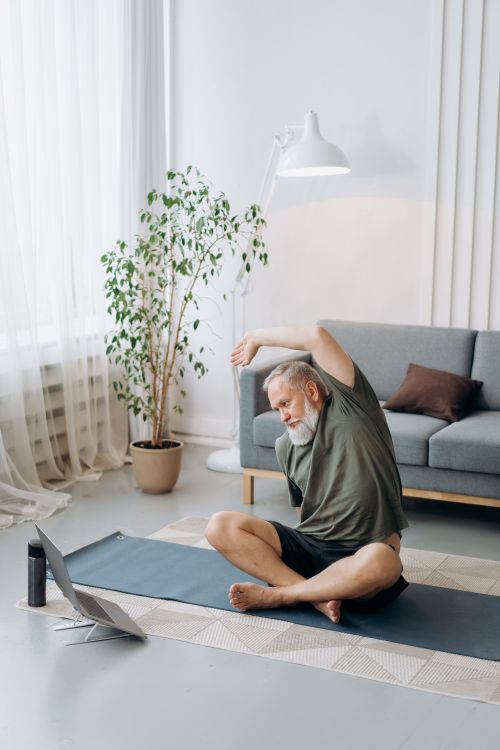 Free Elderly man doing yoga exercises on a mat in the living room, embracing a healthy lifestyle. Stock Photo