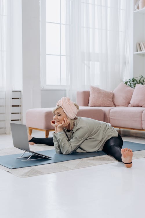 Free An Elderly Woman Looking at Her Laptop while Doing a Leg Split Stock Photo