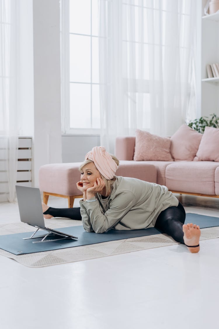 An Elderly Woman Looking At Her Laptop While Doing A Leg Split