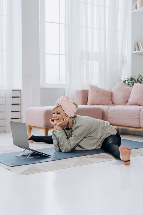 Free Senior woman using a laptop while practicing yoga at home in a bright living room. Stock Photo