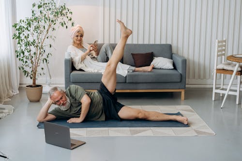 An Elderly Man with His Leg Raised while Looking at the Laptop Screen