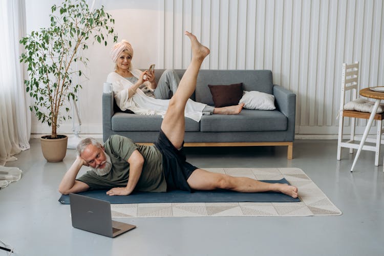 An Elderly Man With His Leg Raised While Looking At The Laptop Screen