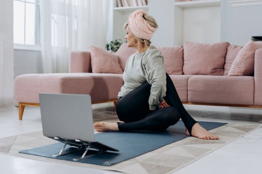 An elderly woman doing yoga indoors with a laptop for guidance, embracing a healthy lifestyle.