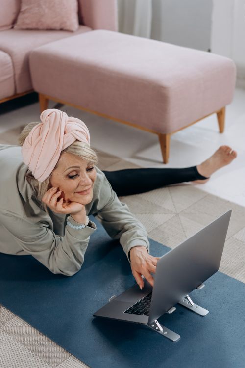 Free Elderly woman with laptop practicing yoga on mat in living room. Stock Photo