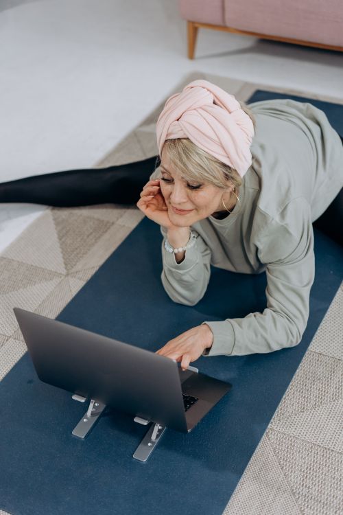 Free A senior woman with a headwrap using a laptop on a yoga mat for online fitness exercises. Stock Photo