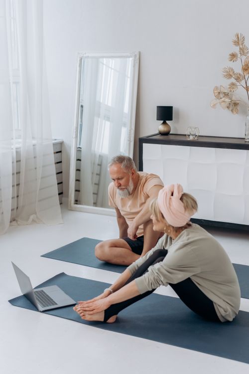 Free Senior couple doing yoga at home with a laptop guide, promoting a healthy lifestyle. Stock Photo
