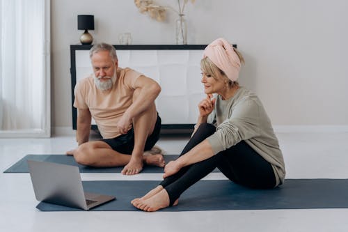 An Elderly Man and Woman Sitting on the Floor while Watching on Laptop
