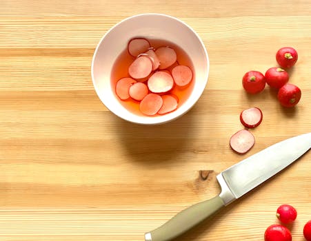 Overhead view of sliced radishes in a bowl with a knife on a wooden surface. Perfect for food photography enthusiasts.