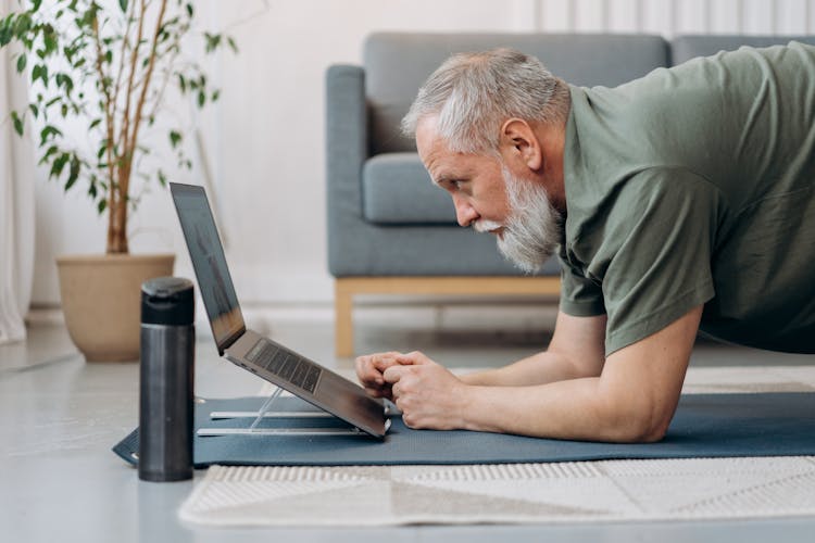 An Elderly Man Working Out While Looking At The Laptop