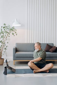 Elderly man doing yoga at home with laptop, promoting active lifestyle and wellness.