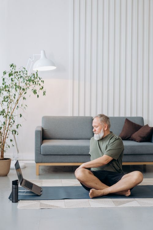 Free Elderly man doing yoga at home with laptop, promoting active lifestyle and wellness. Stock Photo