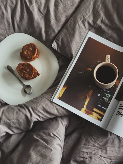 Cup of coffee on magazine near pancakes on plate