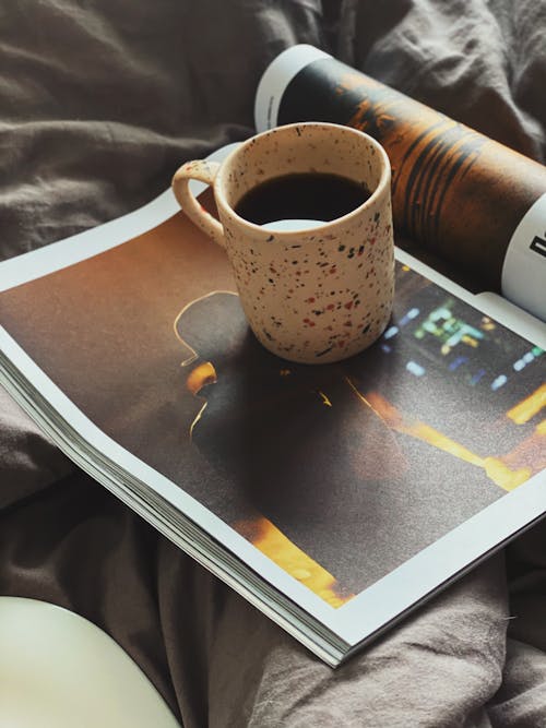 Hot cup of coffee on contemporary magazine placed on blanket