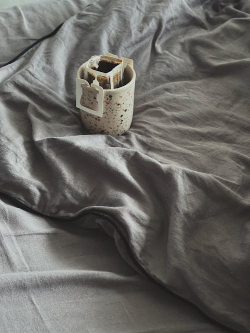 Free From above cup of aromatic freshly brewed drip coffee with paper filter placed on comfortable soft bed in morning Stock Photo