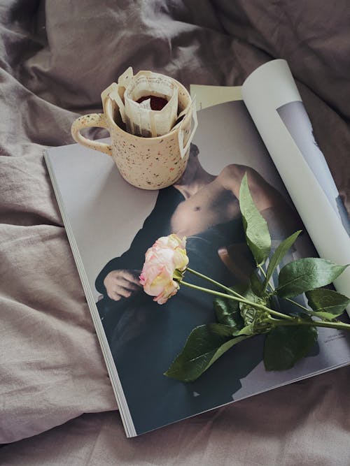 Cup of filtered coffee and rose placed on magazine in bedroom