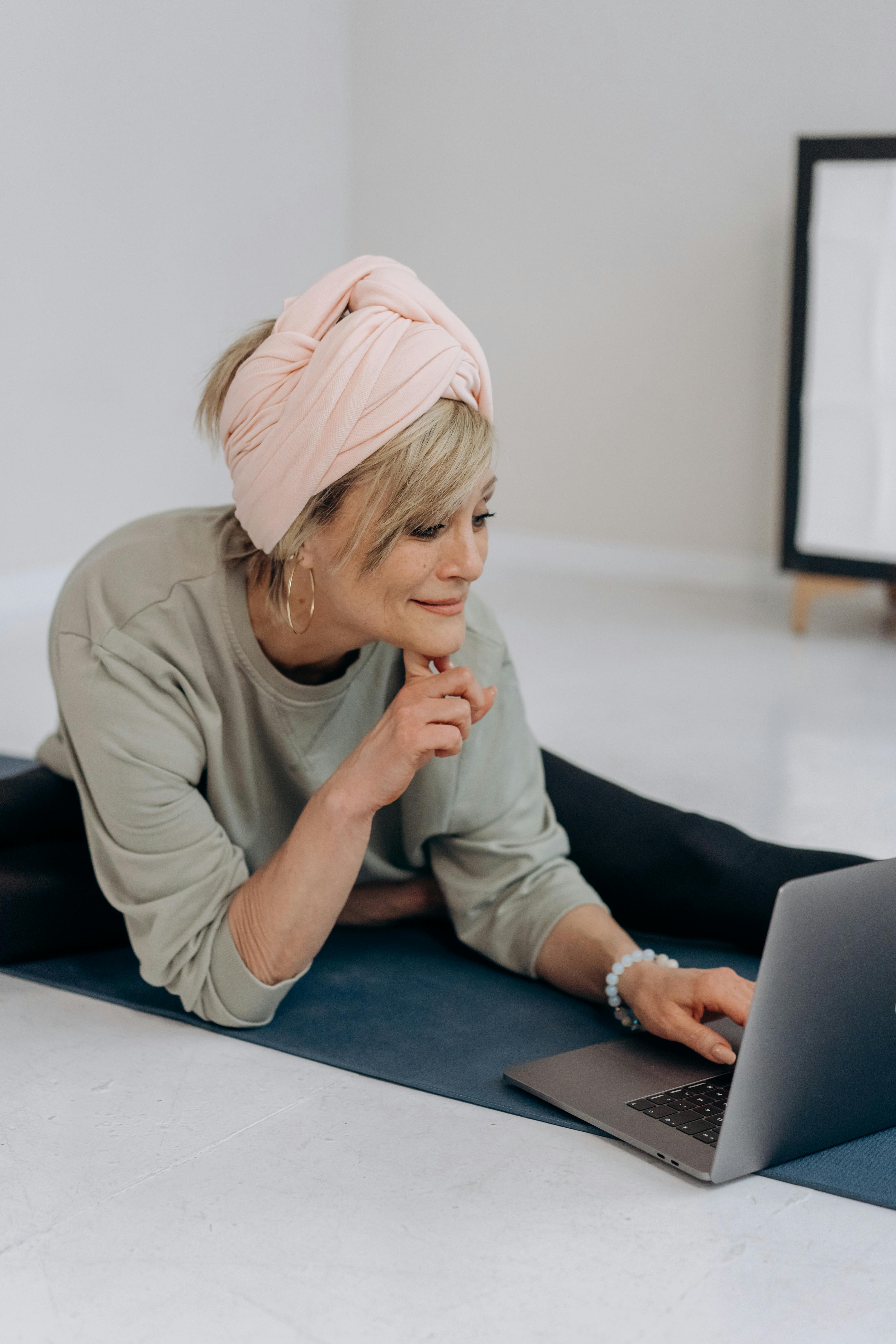 woman sitting on a yoga mat while using laptop