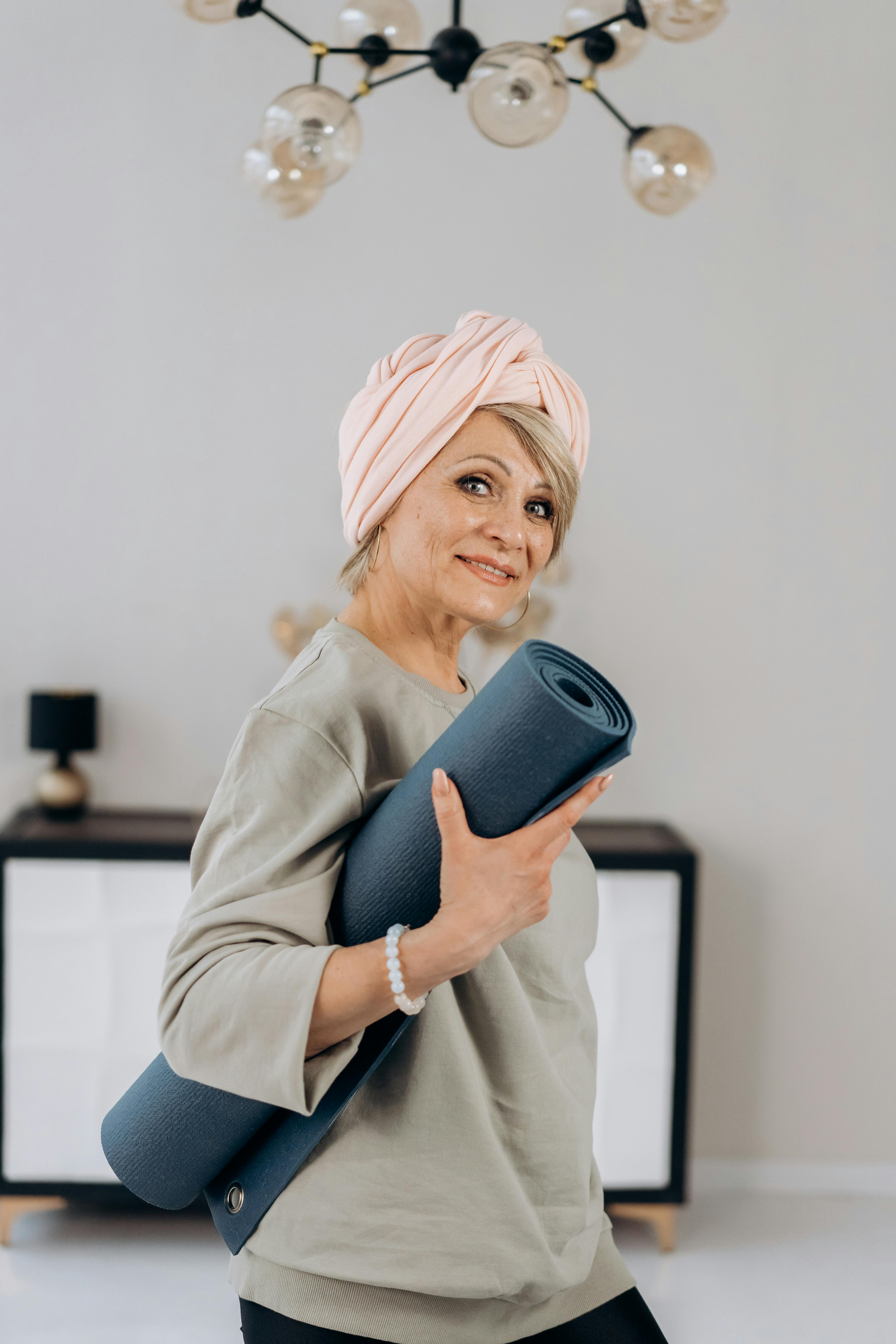 a woman in gray sweater smiling while holding a yoga mat