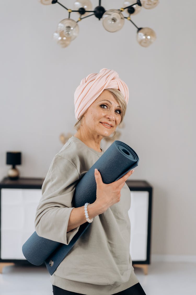 A Woman In Gray Sweater Smiling While Holding A Yoga Mat