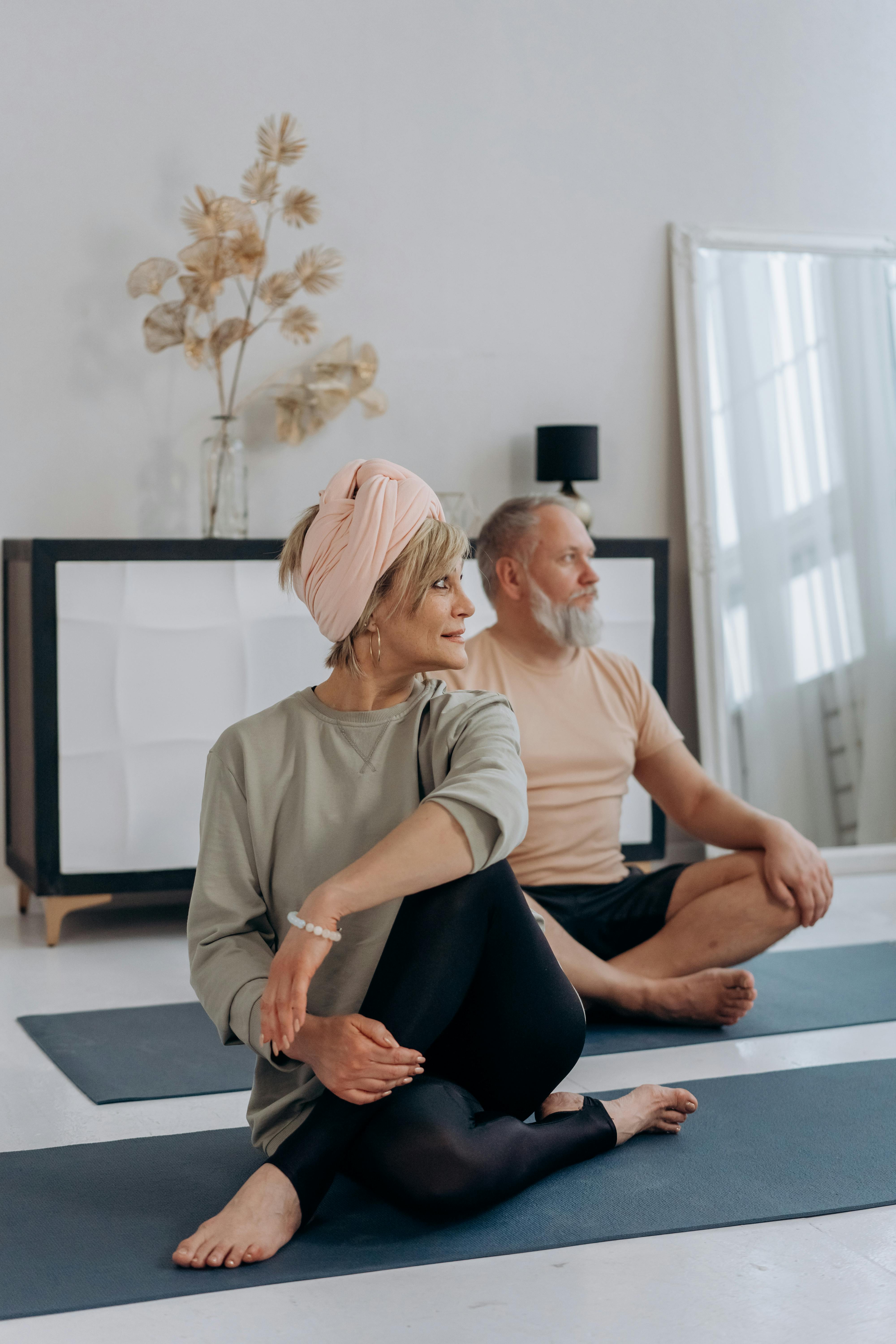 an elderly man and woman sitting on the floor while doing yoga