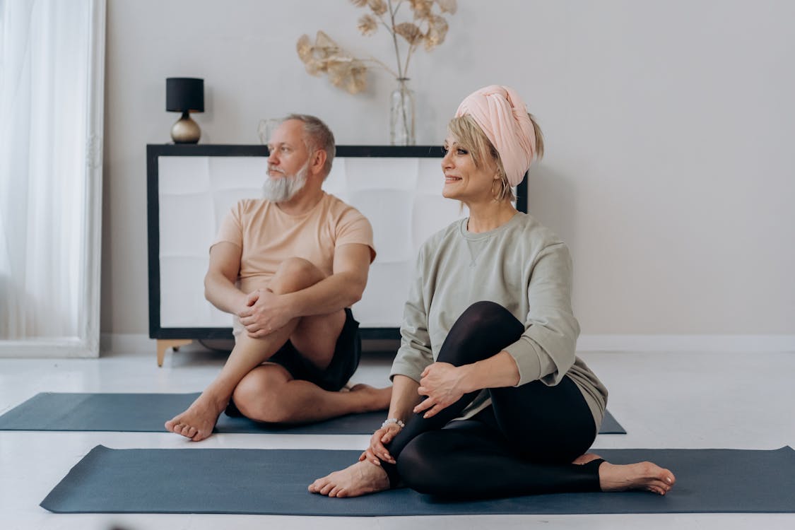 Dois idosos, um homem e uma mulher praticam Pilates sobre um tapete de Yoga.