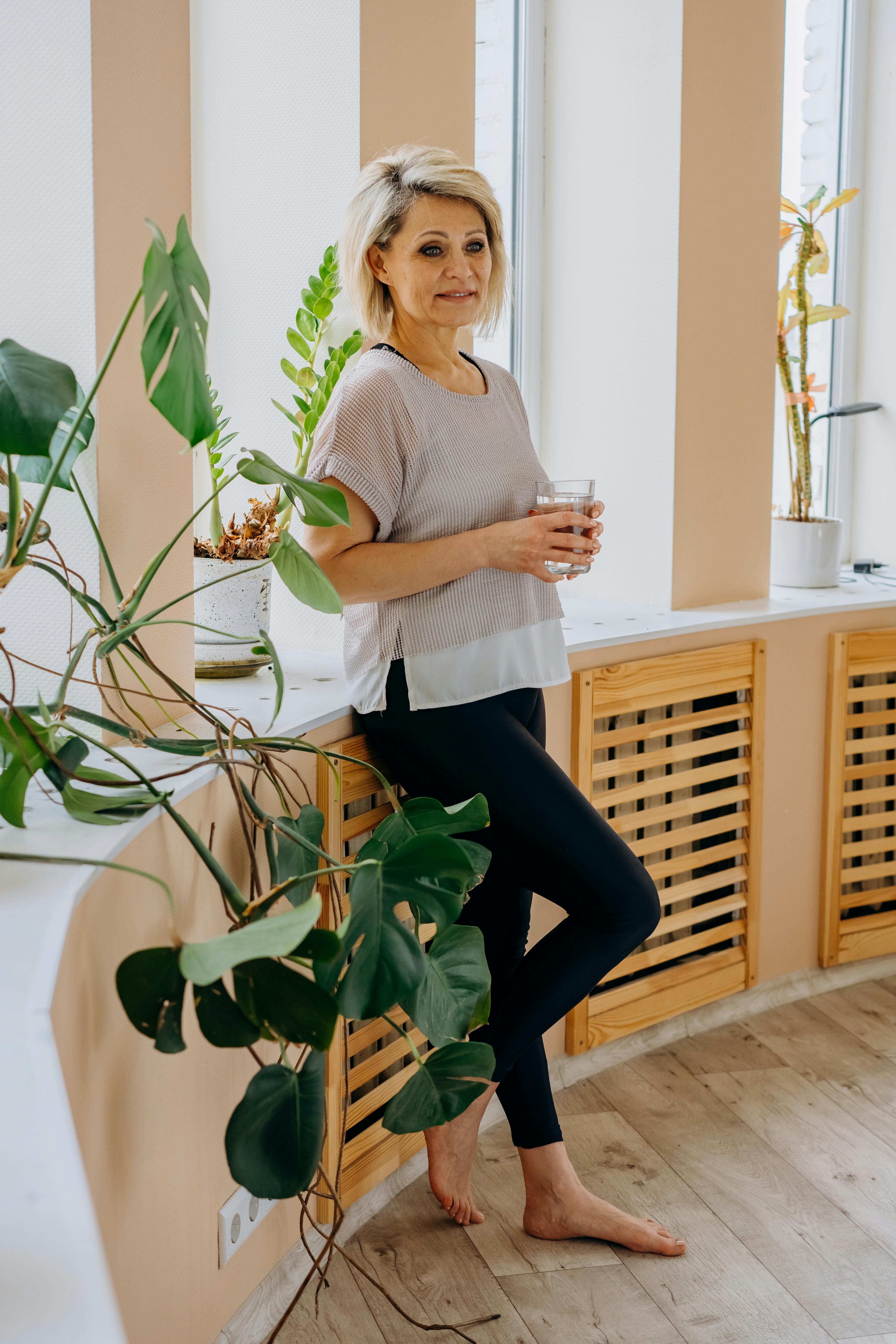 a woman leaning on the windowsill while holding a glass of water