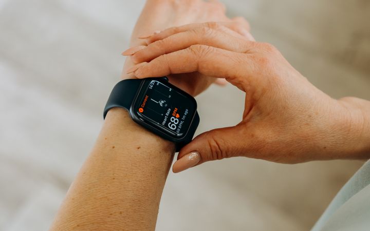 Person interacting with a smartwatch, measuring fitness and heartbeat indoors.