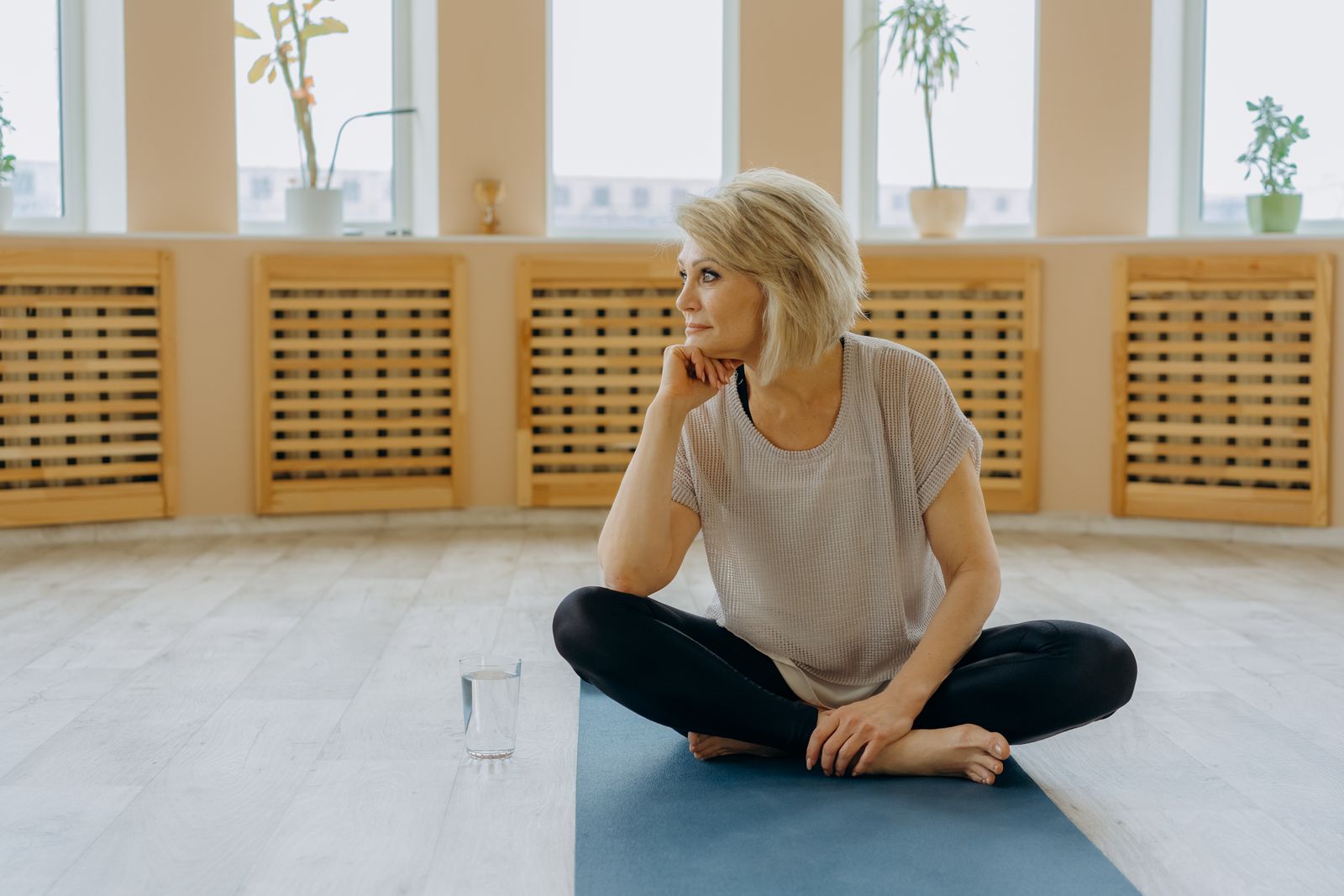 Woman sitting on a yoga mat resting her hand under her chin, practicing face yoga for double chin reduction