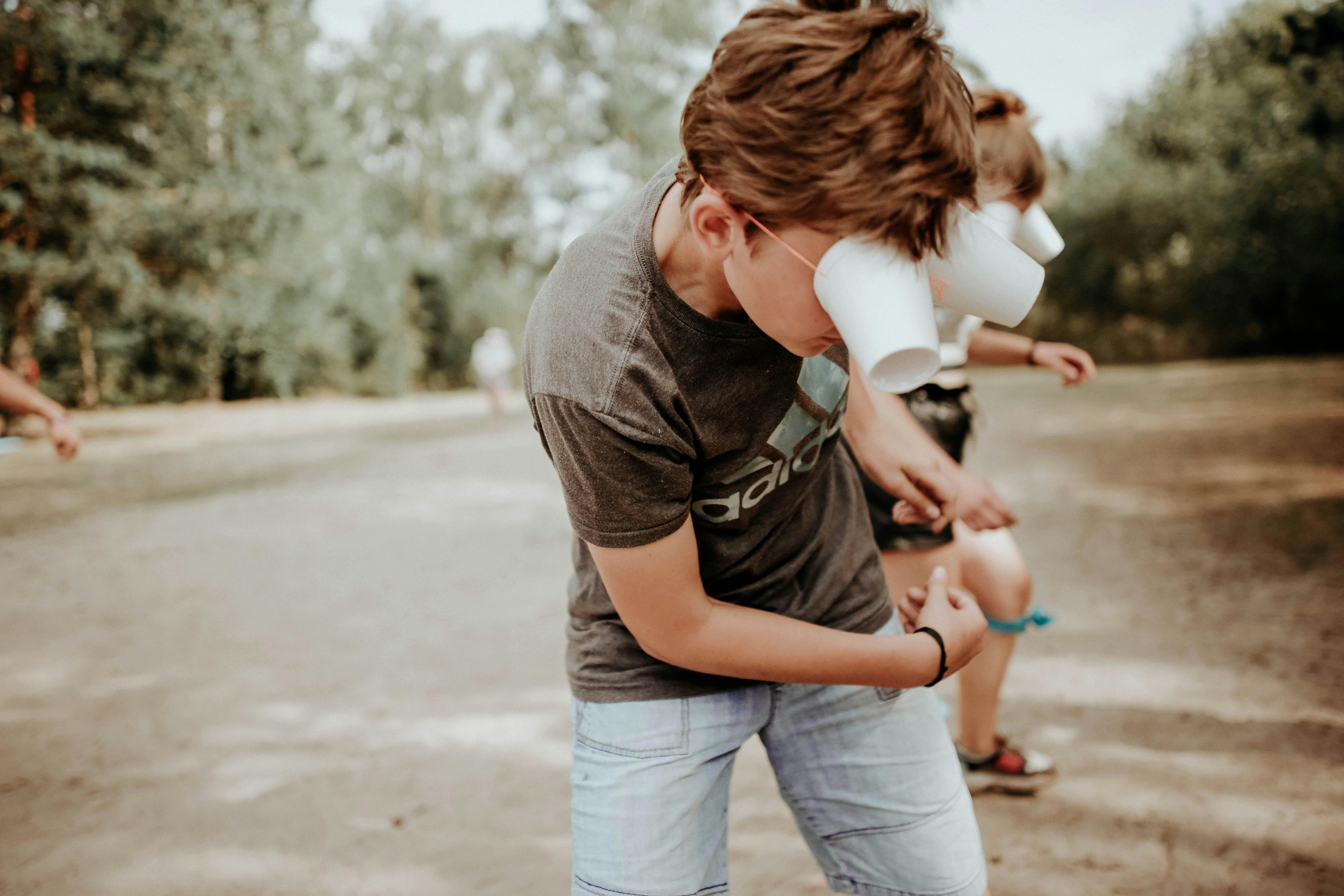 Children playing outdoors with improvised cup eye covers, having fun in a playful setting.