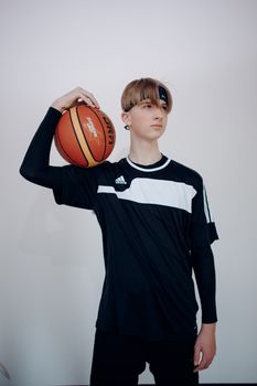 Teen boy holding a basketball in a studio setting, showcasing a sporty pose and expression.