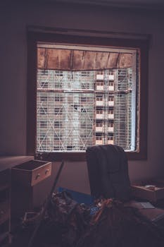 A cluttered room with a view of construction scaffolding through a window, highlighting urban development.