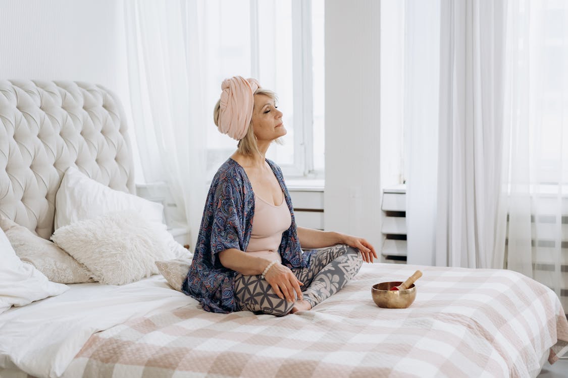 Женщина сидит на кровати с поющей чашей и медитирует