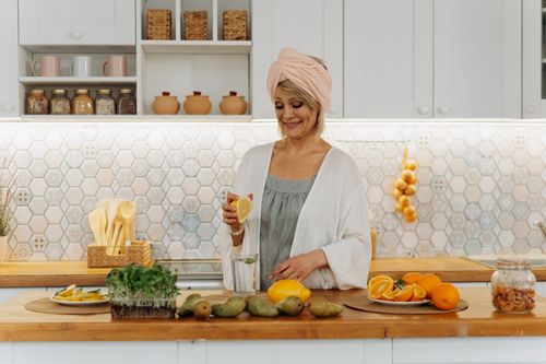 Free Smiling woman squeezing orange in a modern kitchen setting, emphasizing citrus freshness and healthy lifestyle. Stock Photo