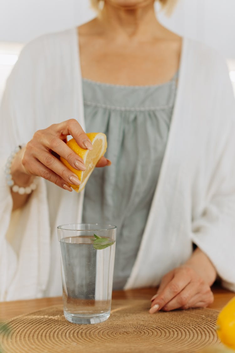 Hand Of A Woman Squeezing Sliced Lemon On Glass Of Water