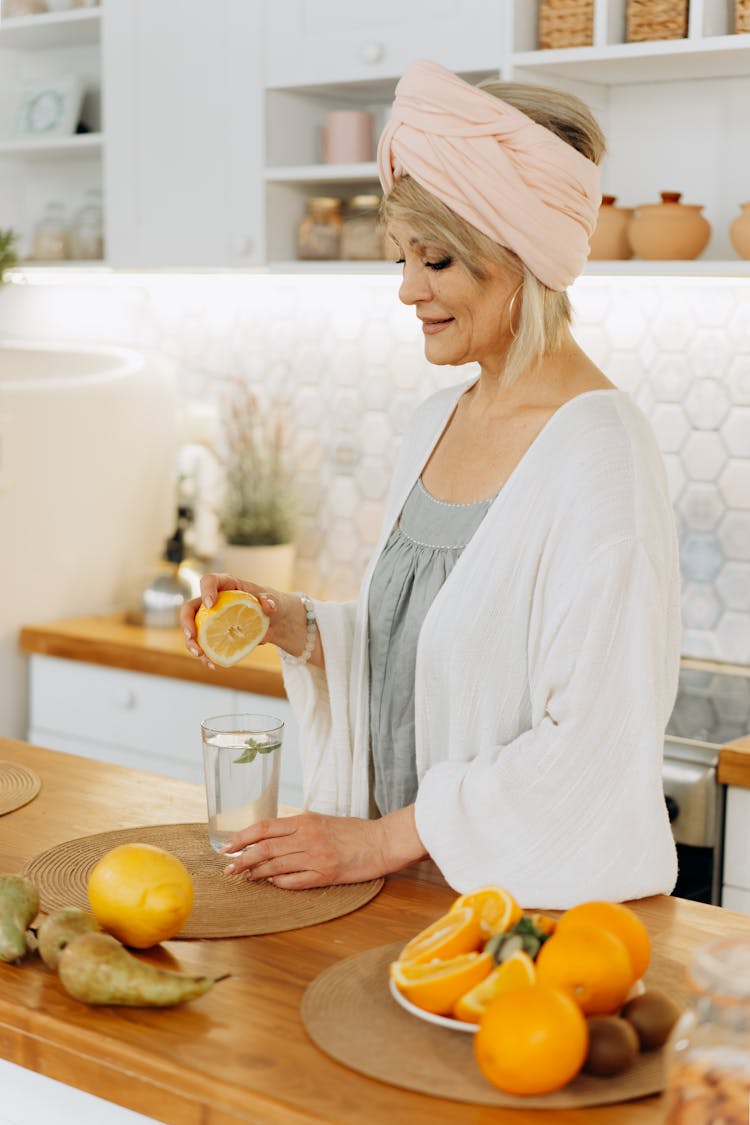 A Mature Woman Squeezing Orange Juice Into A Glass Of Water