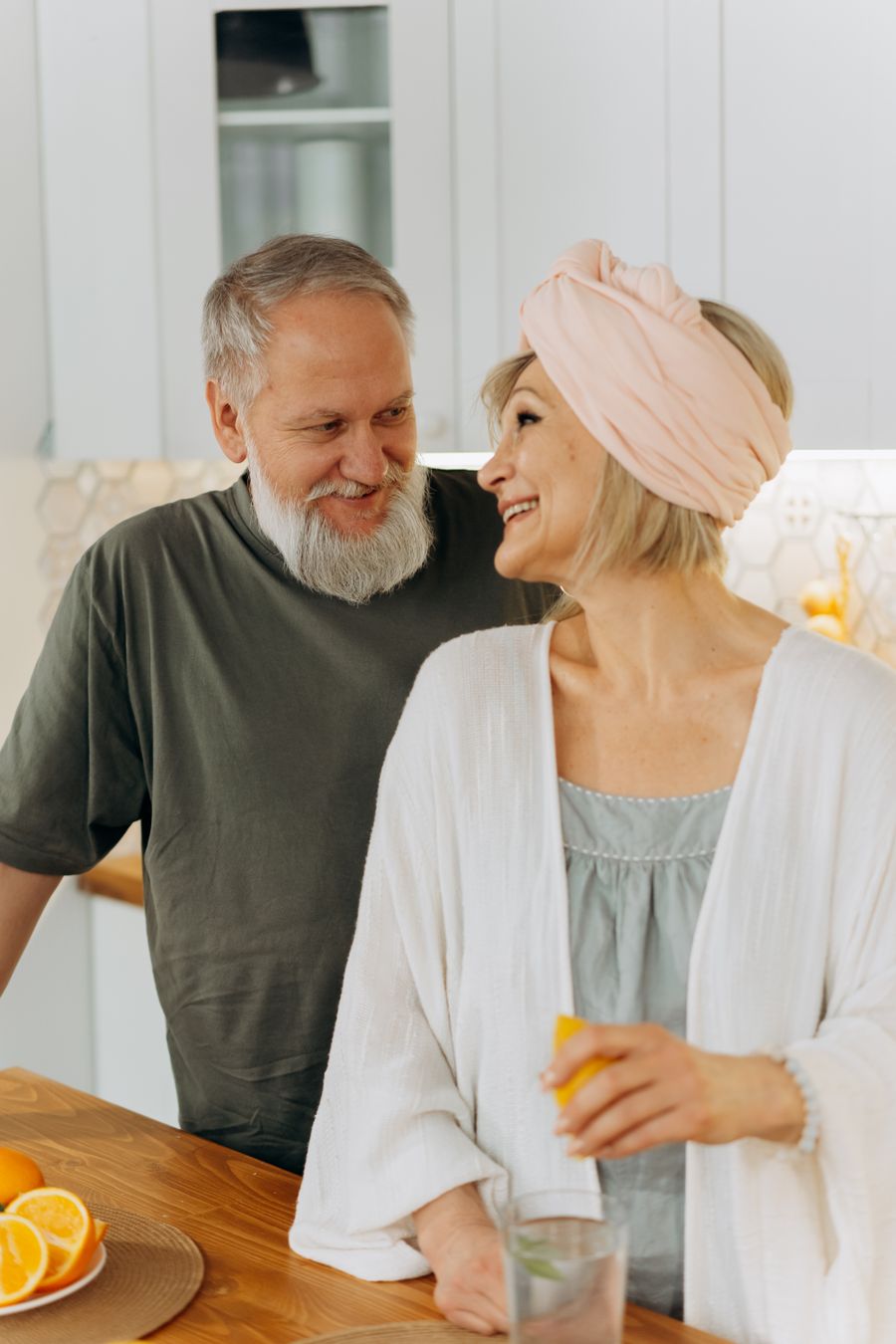 Casal de idosos sorrindo, se olhando com carinho na cozinha de casa