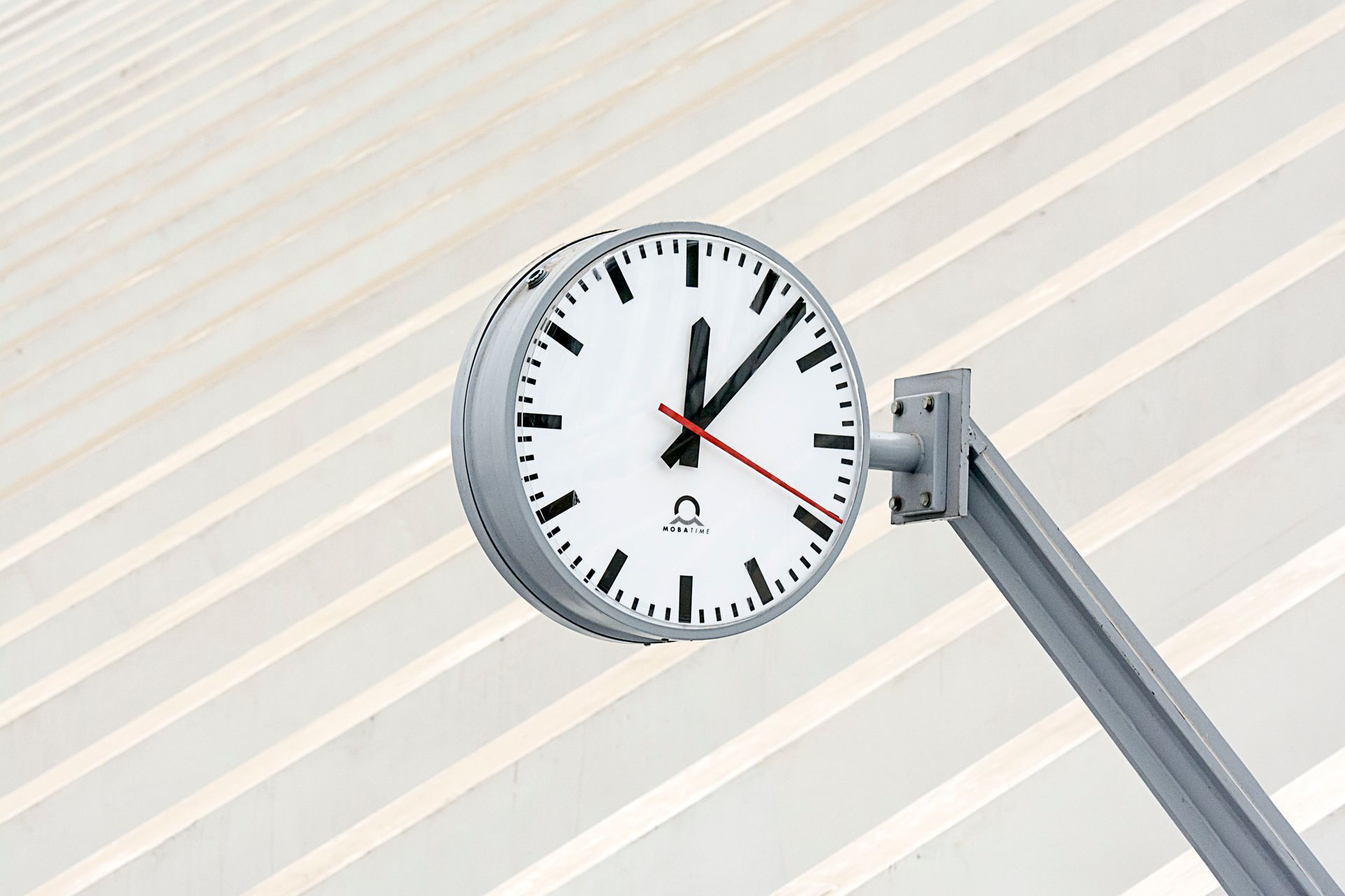 Close-up of a modern clock with a minimalist design against a striped backdrop.