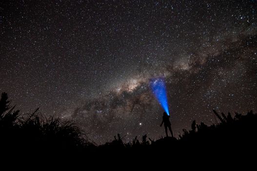 Person with flashlight under the starlit sky of the Milky Way galaxy at night.