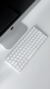 A minimalist workspace featuring a sleek computer and a wireless keyboard on a white desk.
