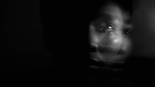 Black and white of unrecognizable person with shade on face in long exposure against dark background
