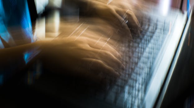 From above of crop anonymous person typing on keyboard of laptop in long exposure