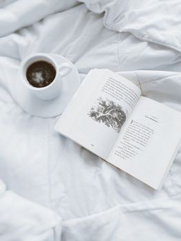 A serene morning scene featuring a cup of coffee and an open book on a soft duvet.