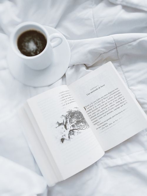 Free A relaxing scene of a cup of coffee and an open book on white bedding. Stock Photo